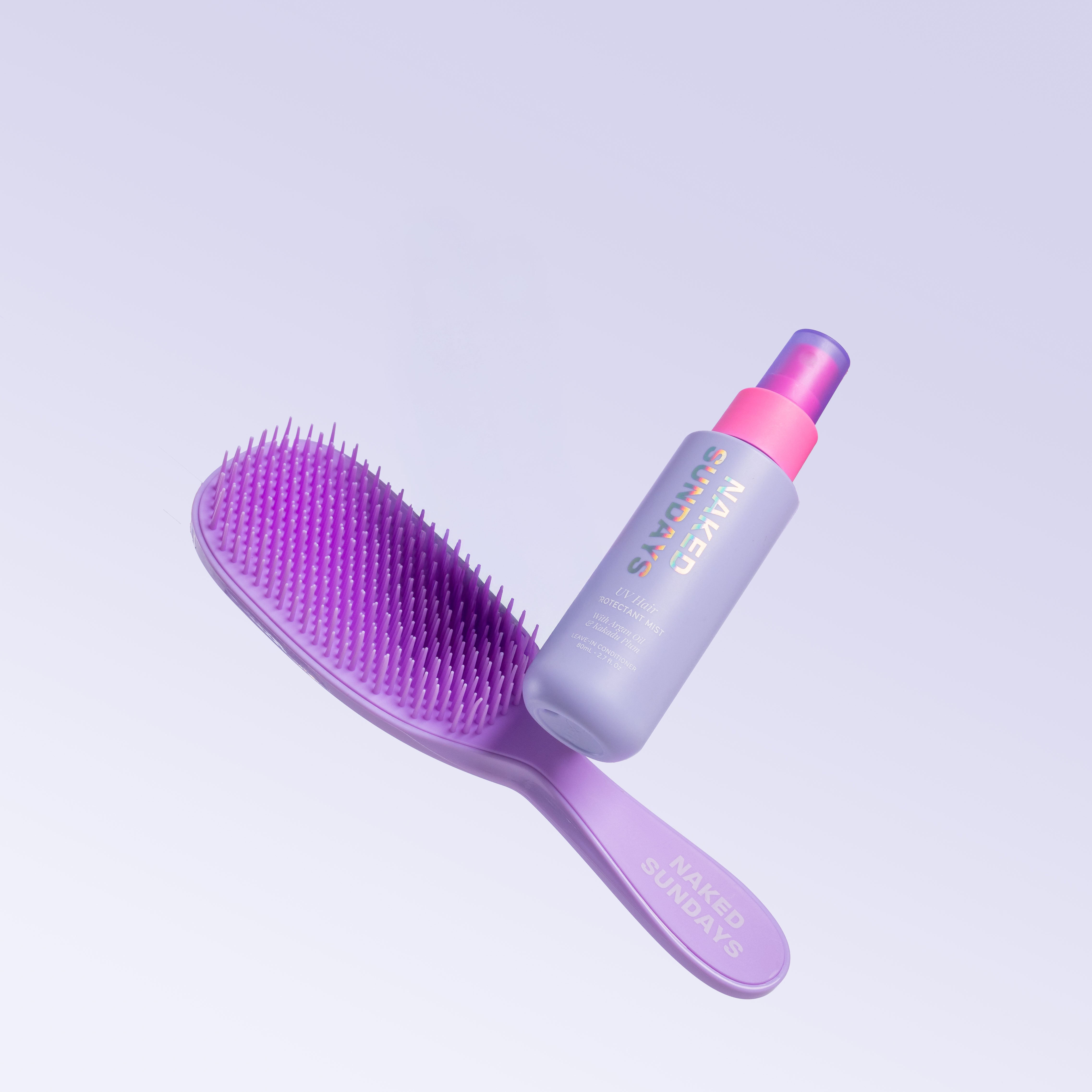 Purple detangling hairbrush and UV Hair mist bottle with pink top on a liliac background