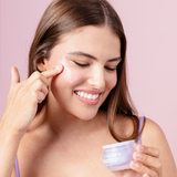 Woman applying face cream to her face with a baby pink background