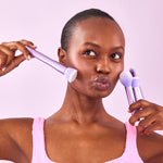 A model holds a set of Naked Sundays purple make up brushes to her face.