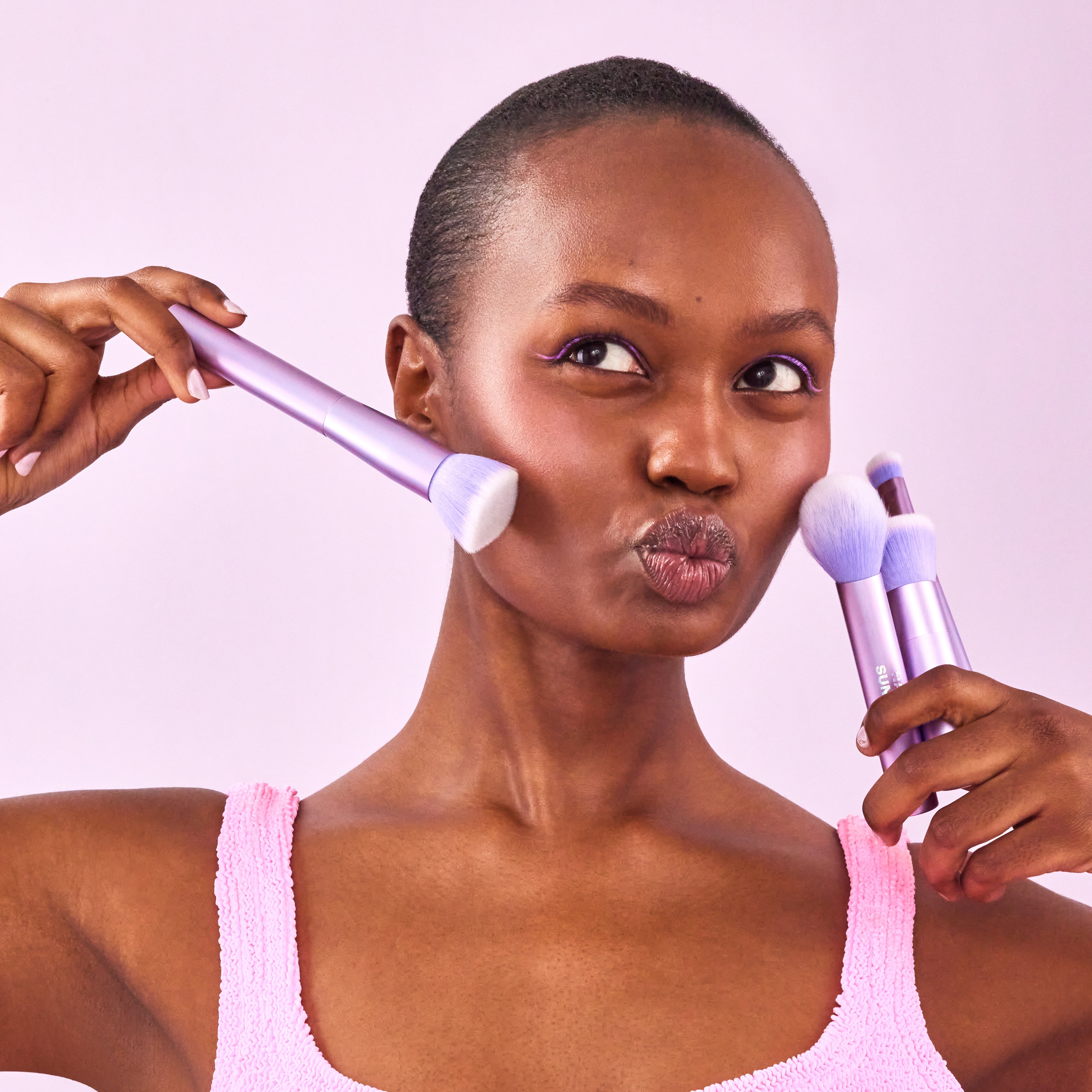 A model holds a set of Naked Sundays purple make up brushes to her face.