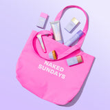 Pink tote bag with 'Naked Sundays' text containing beauty products on a light purple background