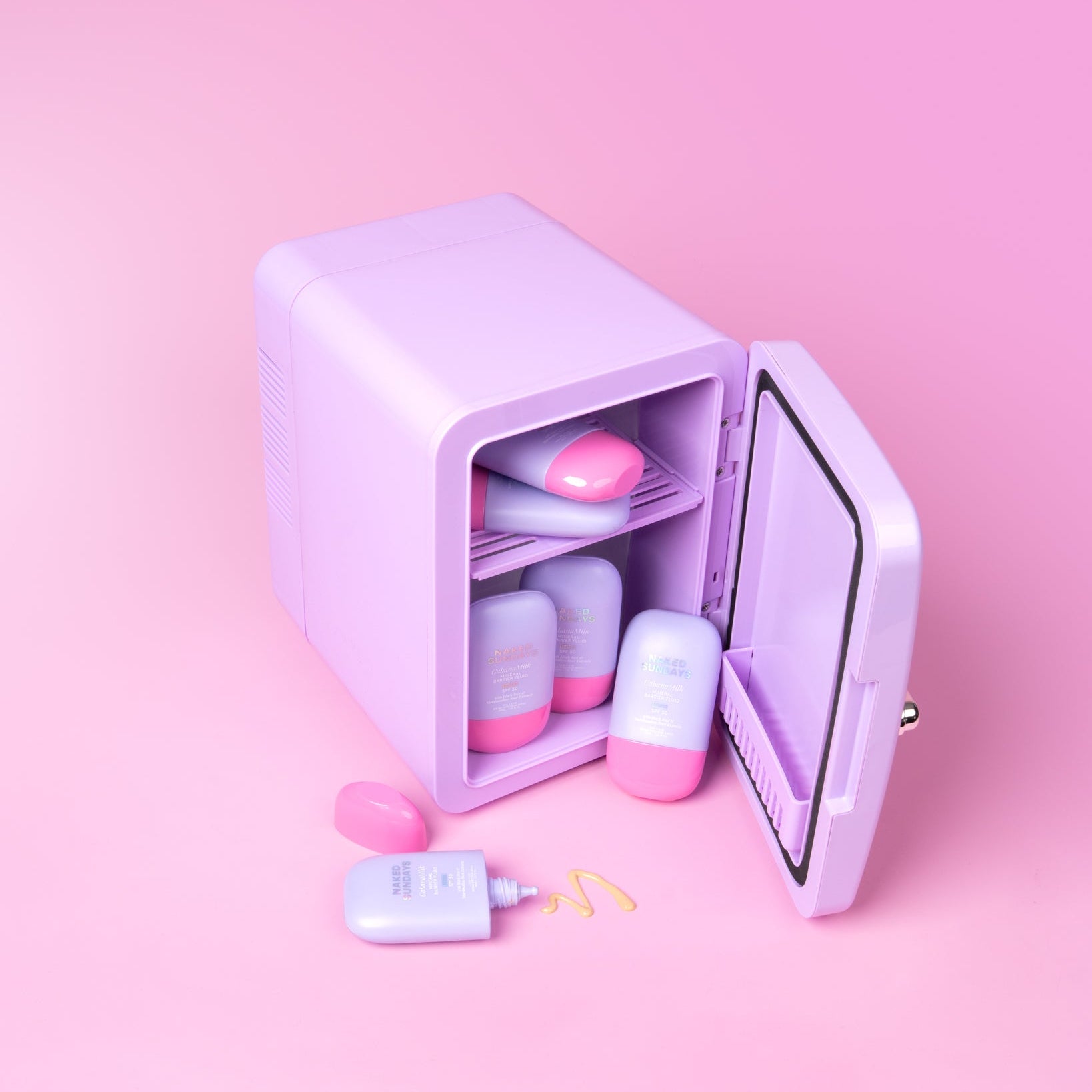 Lilac cosmetics fridge with pink and lilac Cabanamilk SPF50 bottles on a pink background