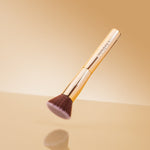 Makeup brush with gold handle and brown bristles on a beige background