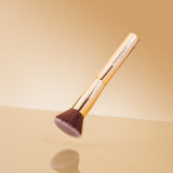 Makeup brush with gold handle and brown bristles on a beige background