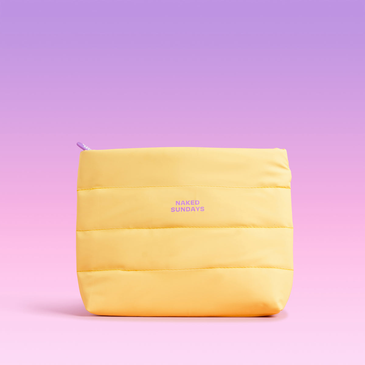 A yellow puffer-style zip pouch with horizontal quilting and the text 'NAKED SUNDAYS' printed in purple on the front, centered against a pink-to-purple gradient background.